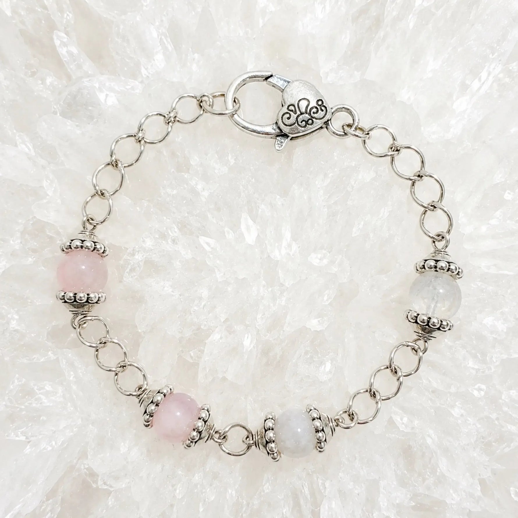 Venus Bracelet featuring rose quartz and moonstone gemstones with sterling silver accents arranged on luminous white quartz crystal.