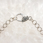 Macro photograph of the Venus Bracelet heart-shaped sterling silver lobster clasp and extension chain resting on white quartz crystal.