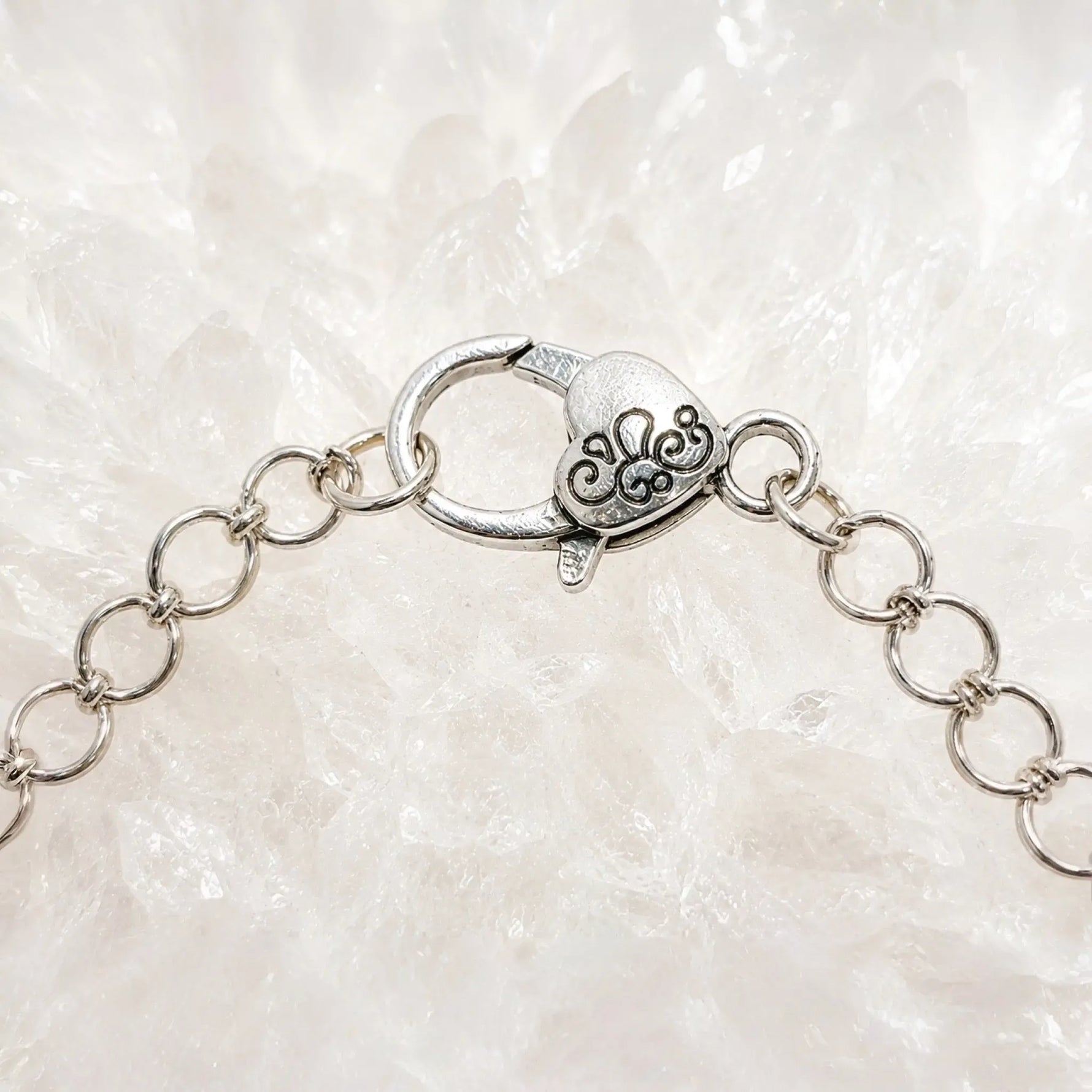 Macro photograph of the Venus Bracelet heart-shaped sterling silver lobster clasp and extension chain resting on white quartz crystal.