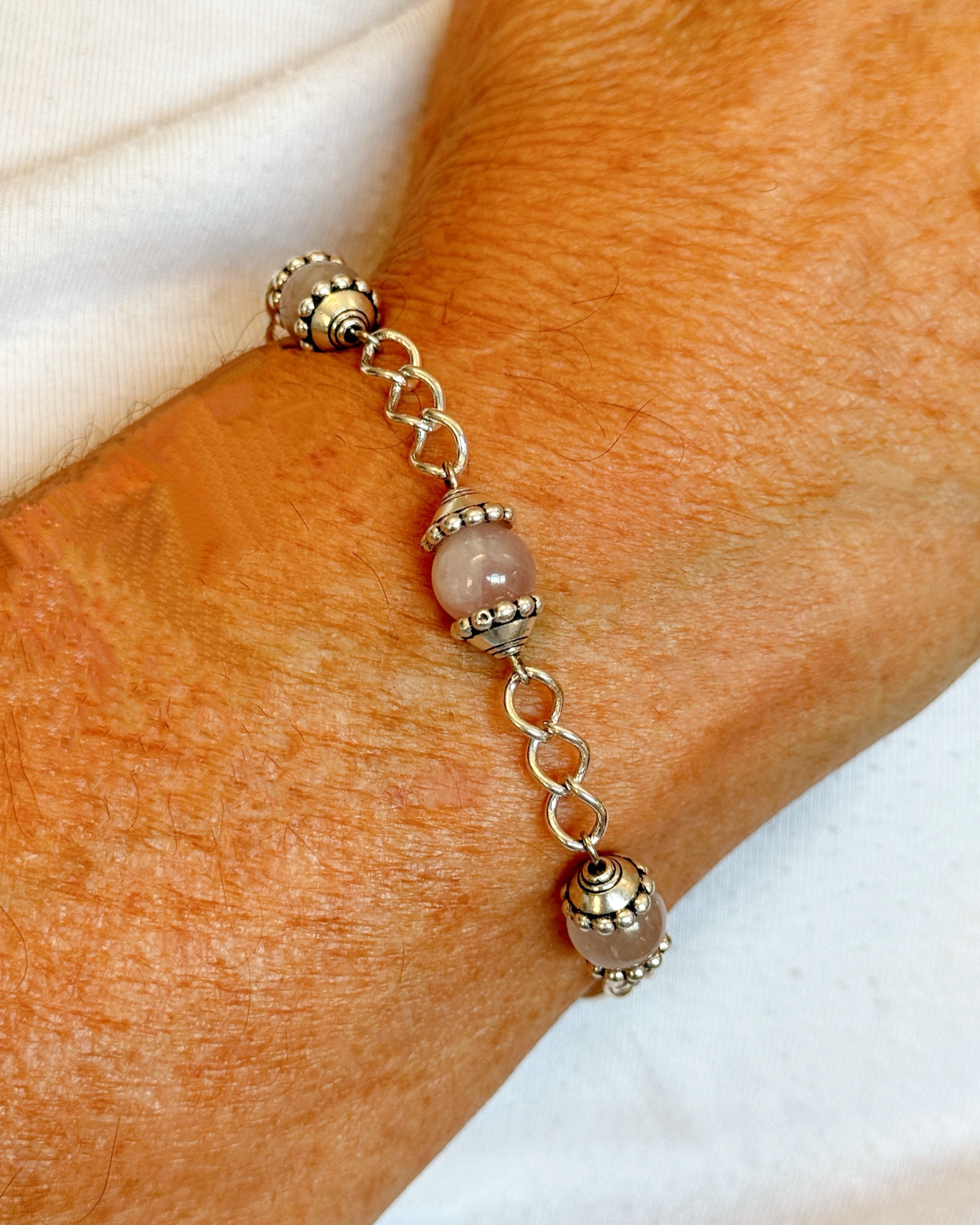 Model wearing the Venus Rose Quartz Bracelet, showcasing rose quartz gemstones, pewter bead caps, and silver-plated curb chain with heart-shaped clasp. Handcrafted in Canada by Carabella by Cheryl.