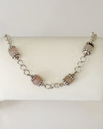 Venus Rose Quartz Bracelet displayed on a jewelry pillow, showing rose quartz gemstone beads, pewter accents, and a silver-plated curb chain with heart clasp.