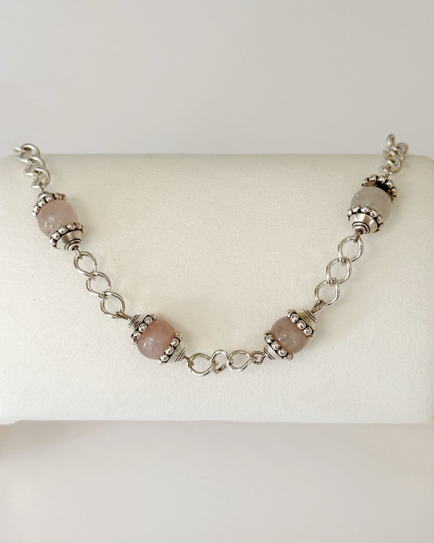 Venus Rose Quartz Bracelet displayed on a jewelry pillow, showing rose quartz gemstone beads, pewter accents, and a silver-plated curb chain with heart clasp.