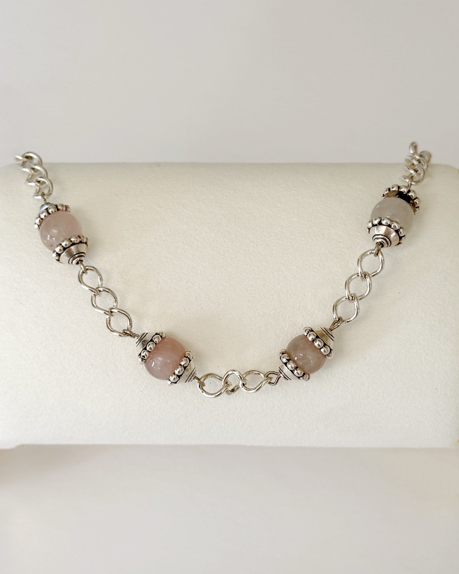 Venus Rose Quartz Bracelet displayed on a jewelry pillow, showing rose quartz gemstone beads, pewter accents, and a silver-plated curb chain with heart clasp.
