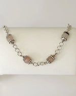 Venus Rose Quartz Bracelet displayed on a jewelry pillow, showing rose quartz gemstone beads, pewter accents, and a silver-plated curb chain with heart clasp.
