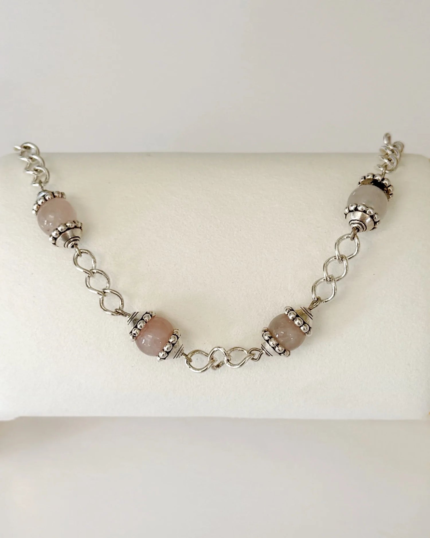 Venus Rose Quartz Bracelet displayed on a jewelry pillow, showing rose quartz gemstone beads, pewter accents, and a silver-plated curb chain with heart clasp.