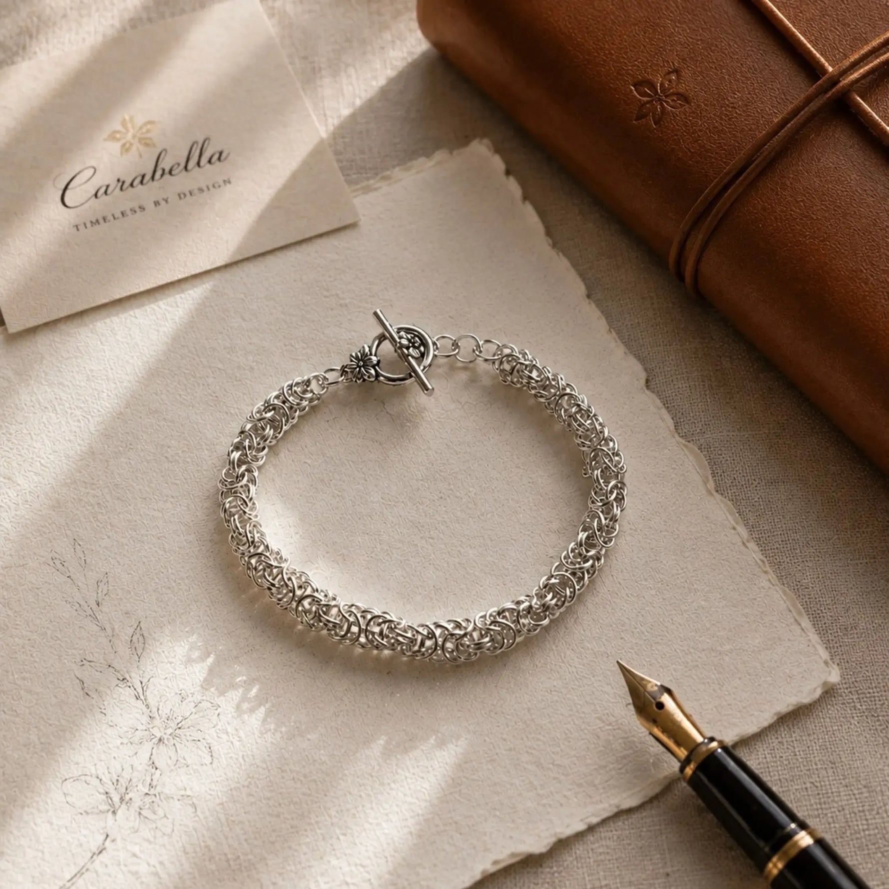 Zoe sterling silver Byzantine weave bracelet presented on ivory linen beside a leather journal and fountain pen in a heritage-inspired editorial flat lay.