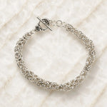 Zoe sterling silver Byzantine weave bracelet handcrafted in Canada with floral toggle clasp on Carabella quartz surface.