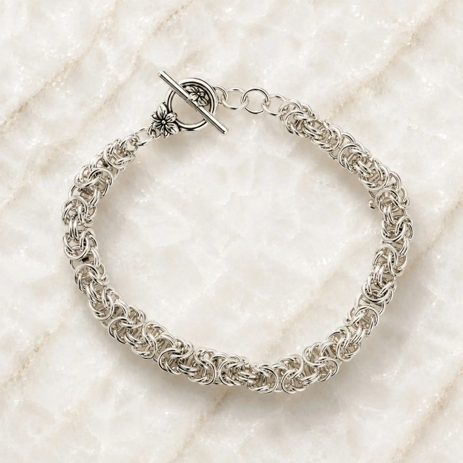 Zoe sterling silver Byzantine weave bracelet handcrafted in Canada with floral toggle clasp on Carabella quartz surface.