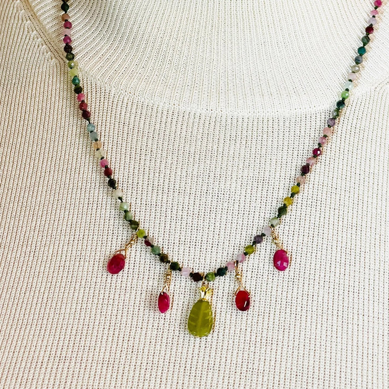 Model wearing the Layla Gemstone Necklace with rainbow tourmaline, ruby drops, and a carved jade leaf pendant styled over a neutral knit top.